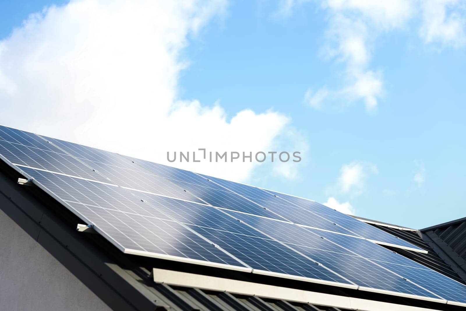 Solar panel cells on cloudy blue sky background. Clean alternative energy power concept. Modern house with solar panels stand-alone photovoltaic plant system on metal sheet roof. Go green