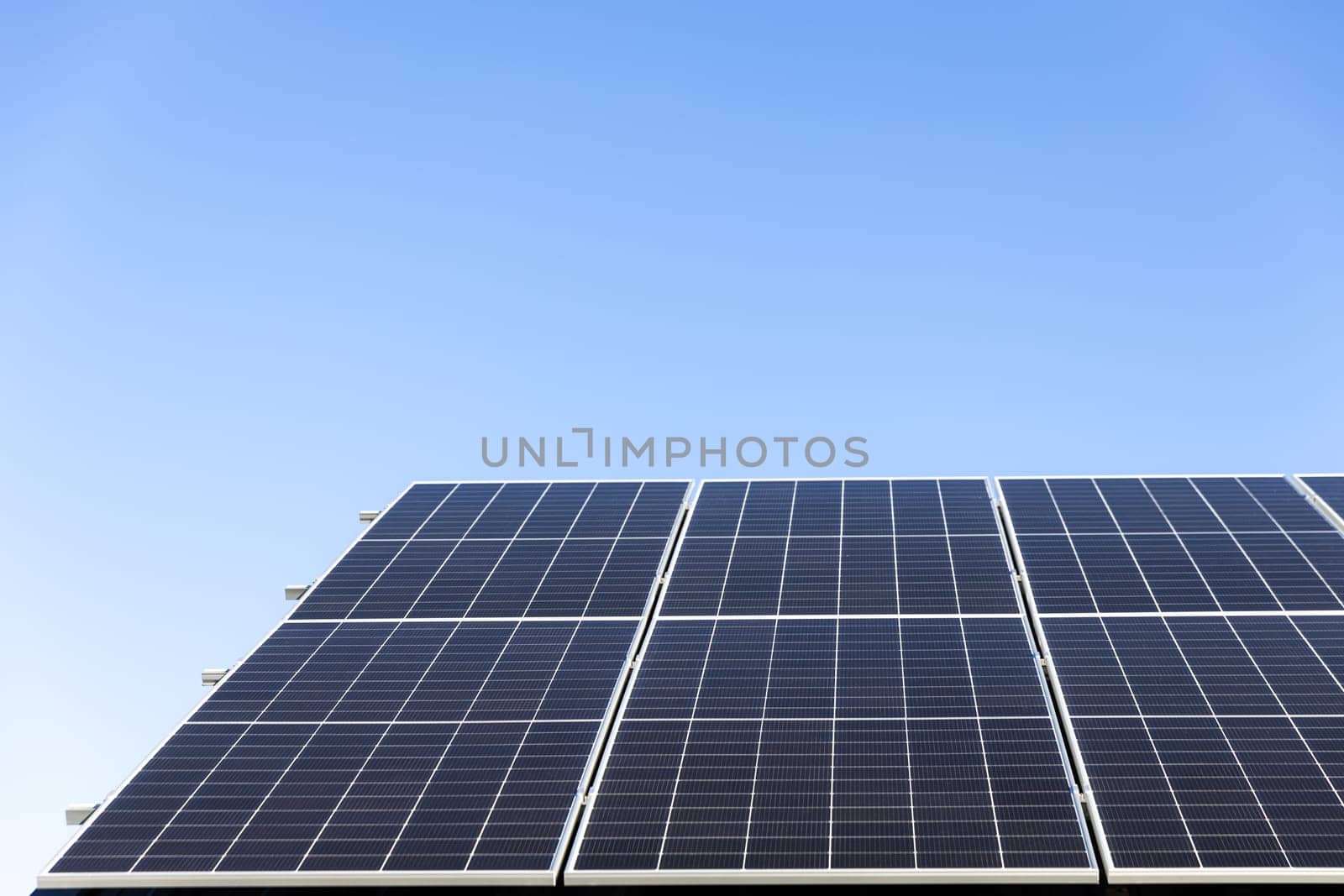 Aerial view of solar panel cells on clear blue sky background. Clean alternative energy power concept, sustainable resources. Modern house, solar panels stand-alone photovoltaic plant system on roof