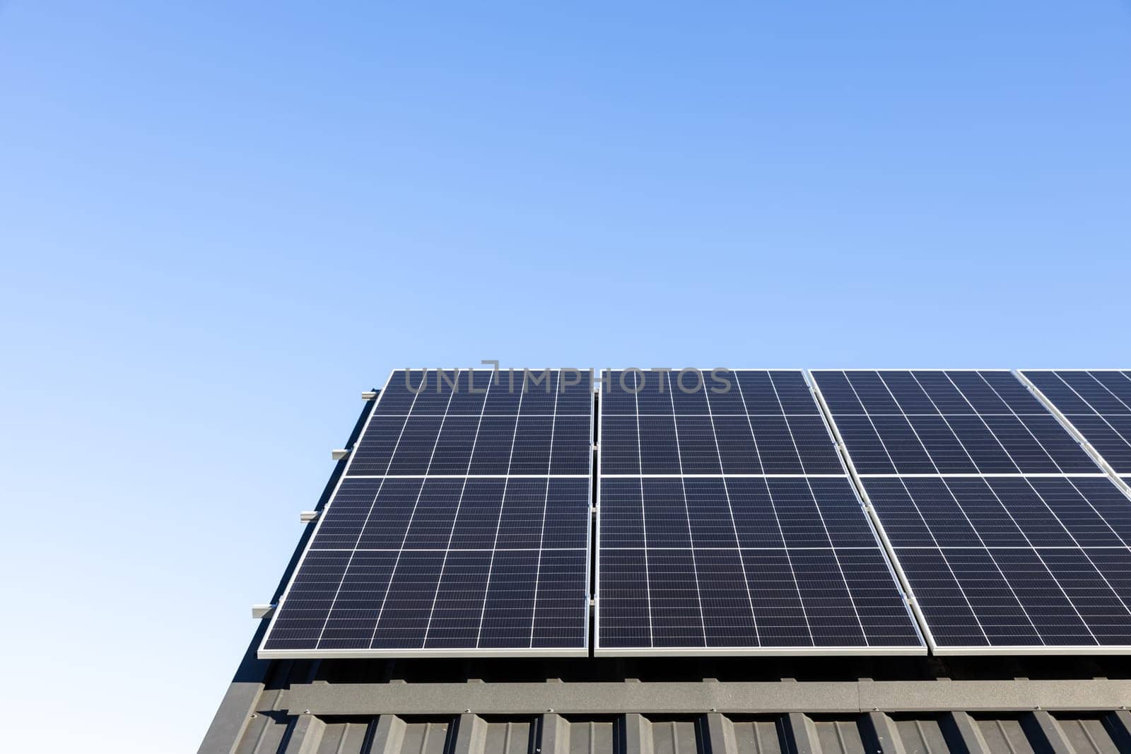 Modern house with solar panels stand-alone photovoltaic plant system on household metal sheet roof. Clear blue sky background. Clean alternative energy power concept, sustainable resources