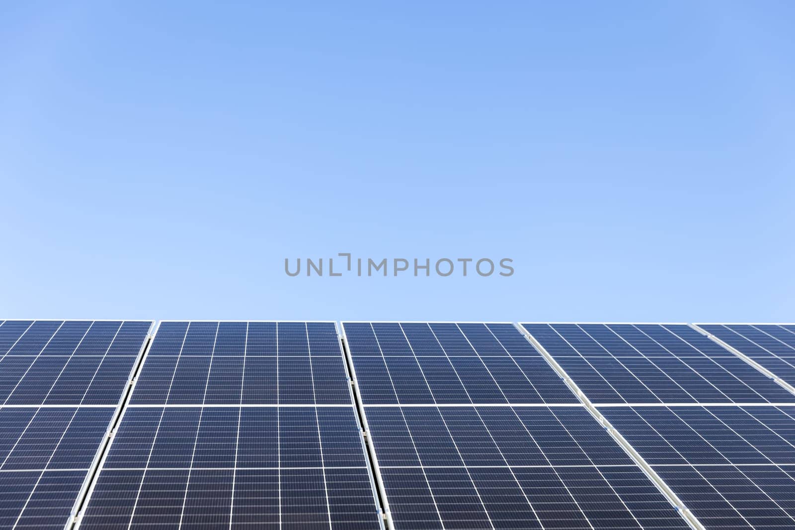 Aerial view of solar panel cells on clear blue sky background. Clean alternative energy power concept, sustainable resources. Modern house, solar panels stand-alone photovoltaic plant system on roof