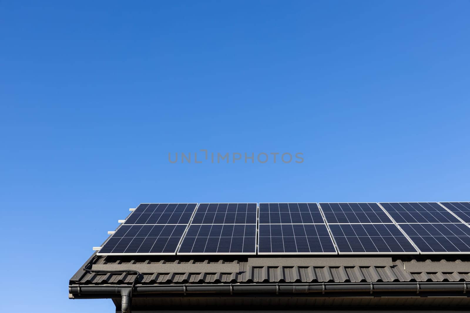 House with solar panels photovoltaic plant system professionally installed on metal sheet roof, go green. Clear blue sky background. Clean alternative energy power concept, sustainable resources
