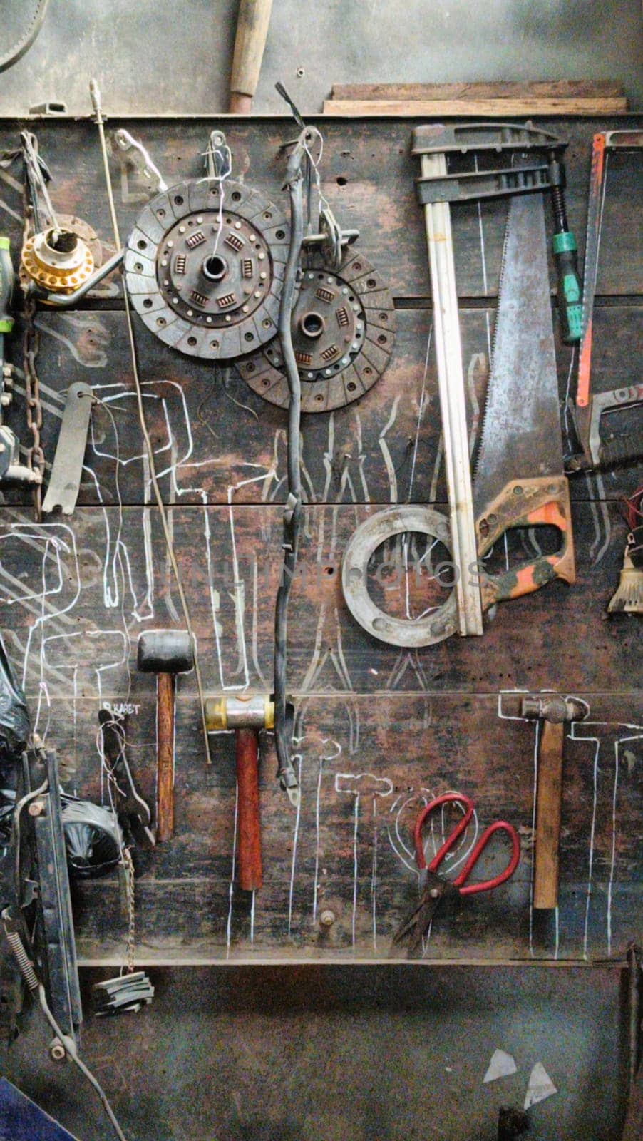A cluttered workshop scene showcasing an assortment of tools hanging on a wooden wall and surrounding shelves, creating a rustic and industrial atmosphere.