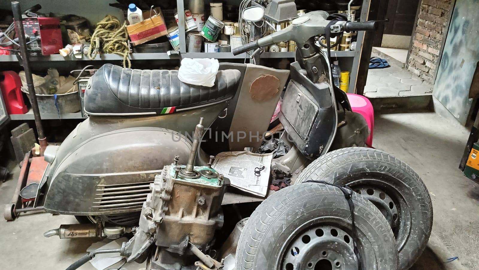 A classic scooter and various spare parts in an old workshop setting. The scene suggests machinery repair, vintage restoration, and mechanical work, symbolizing nostalgia and automotive passion.