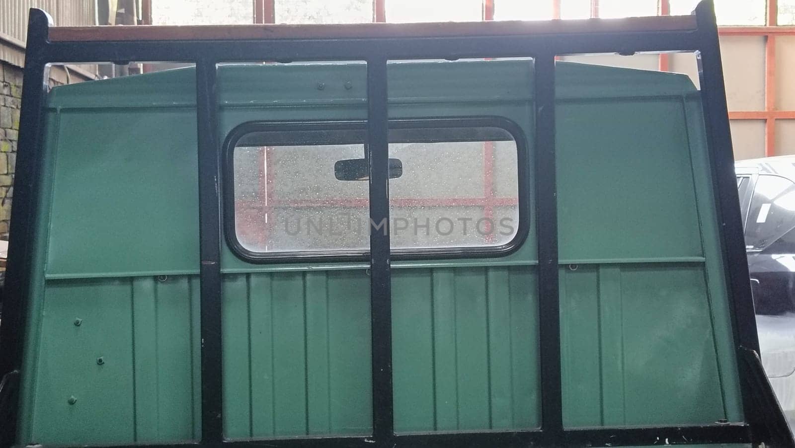An empty green pickup truck bed inside an industrial garage featuring parked vehicles and storage. Captures the essence of vintage utility and automotive design.