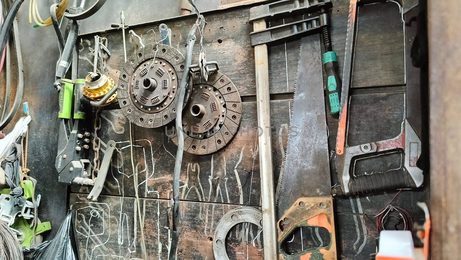 A cluttered workshop scene showcasing an assortment of tools hanging on a wooden wall and surrounding shelves, creating a rustic and industrial atmosphere.