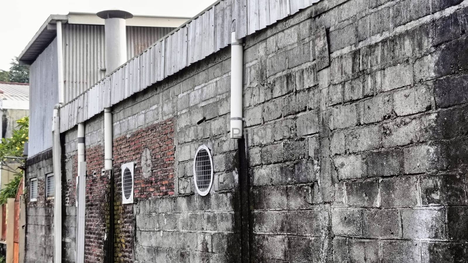 An industrial building partially hidden by a brick wall under a blue sky. The image captures urban architecture with a mix of materials and textures in a relaxed setting.