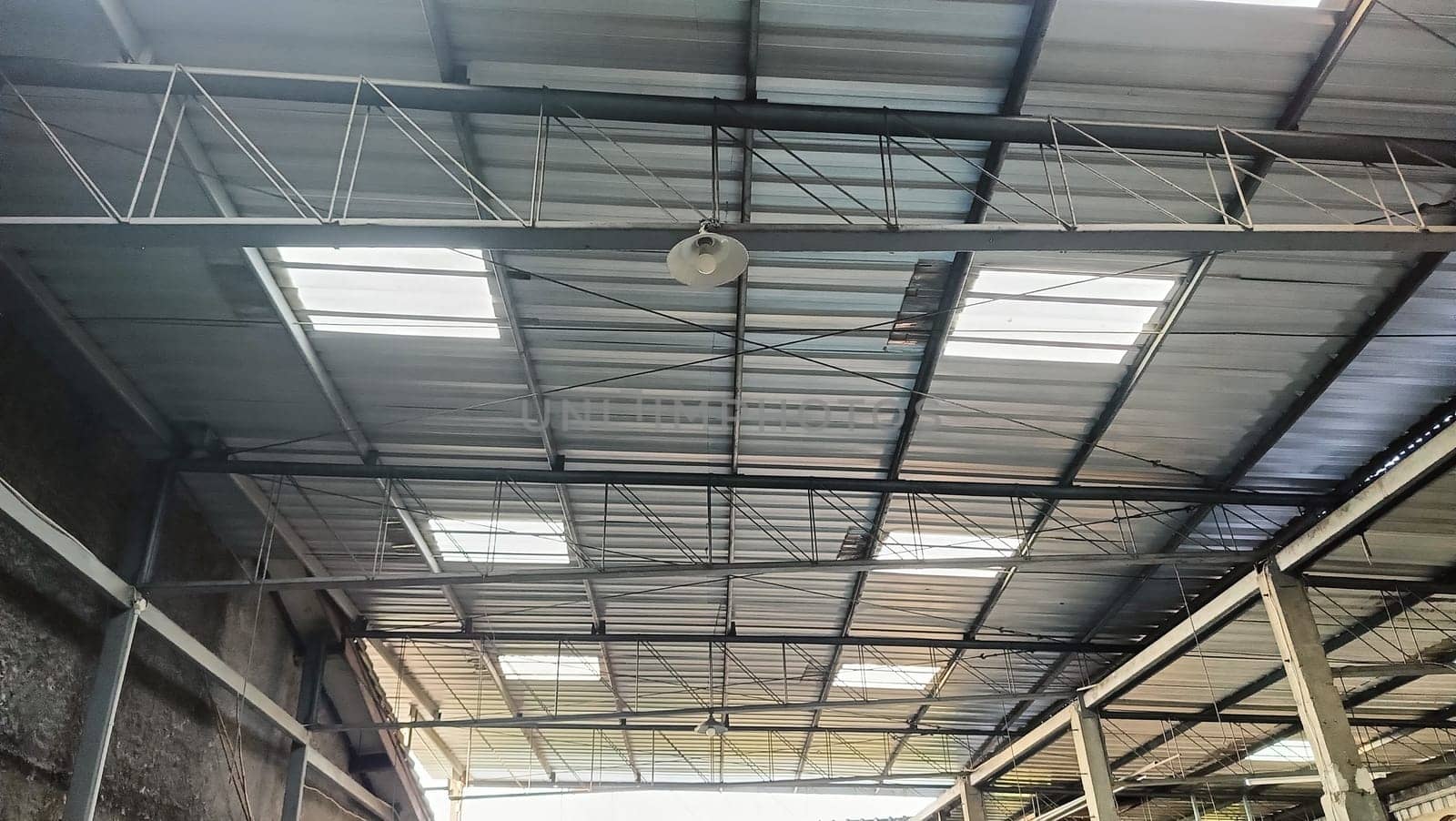 View of a sturdy metal roof with beams inside a spacious warehouse. The structure depicts industrial architecture, showcasing strength and functionality. This space is ideal for storage and manufacturing.