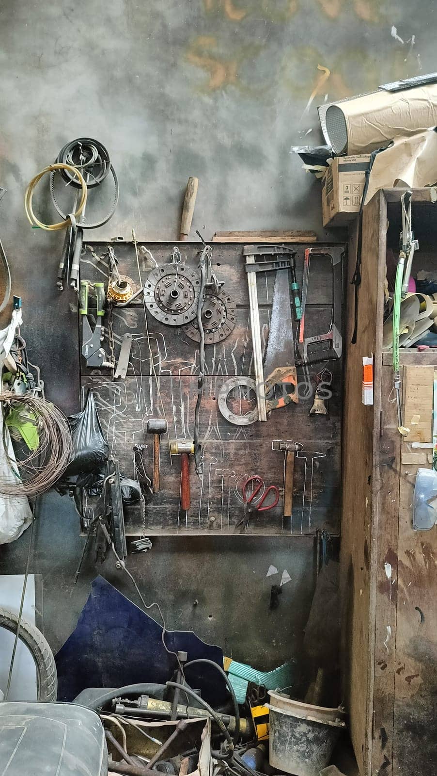 A cluttered workshop scene showcasing an assortment of tools hanging on a wooden wall and surrounding shelves, creating a rustic and industrial atmosphere.