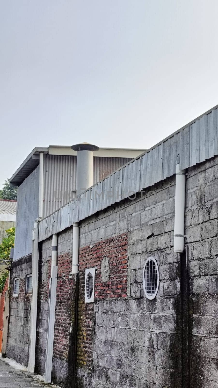 An industrial building partially hidden by a brick wall under a blue sky. The image captures urban architecture with a mix of materials and textures in a relaxed setting.