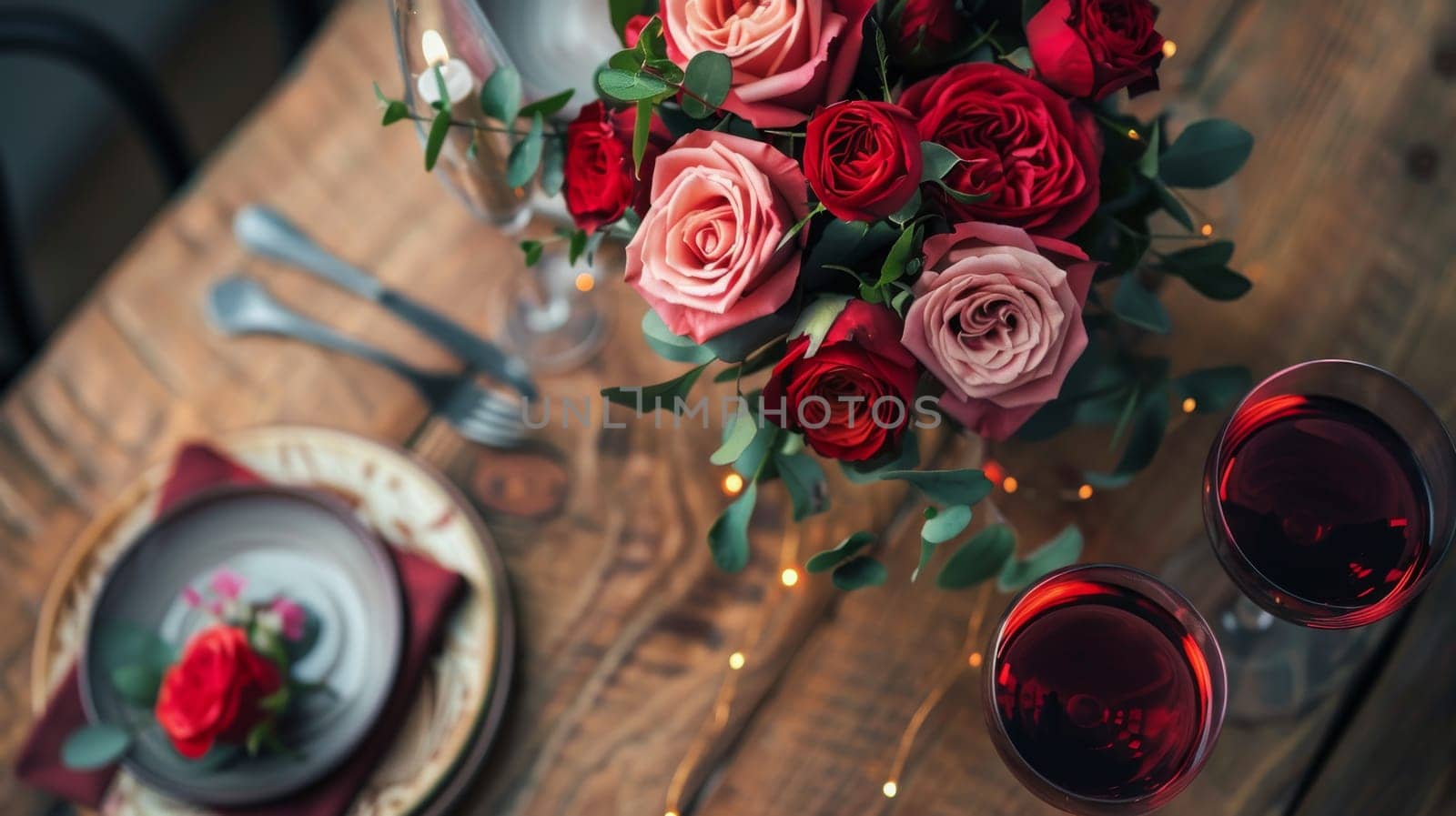 A romantic dinner setup with wine glasses and a bouquet of roses on a rustic wooden table, captured from a high angle