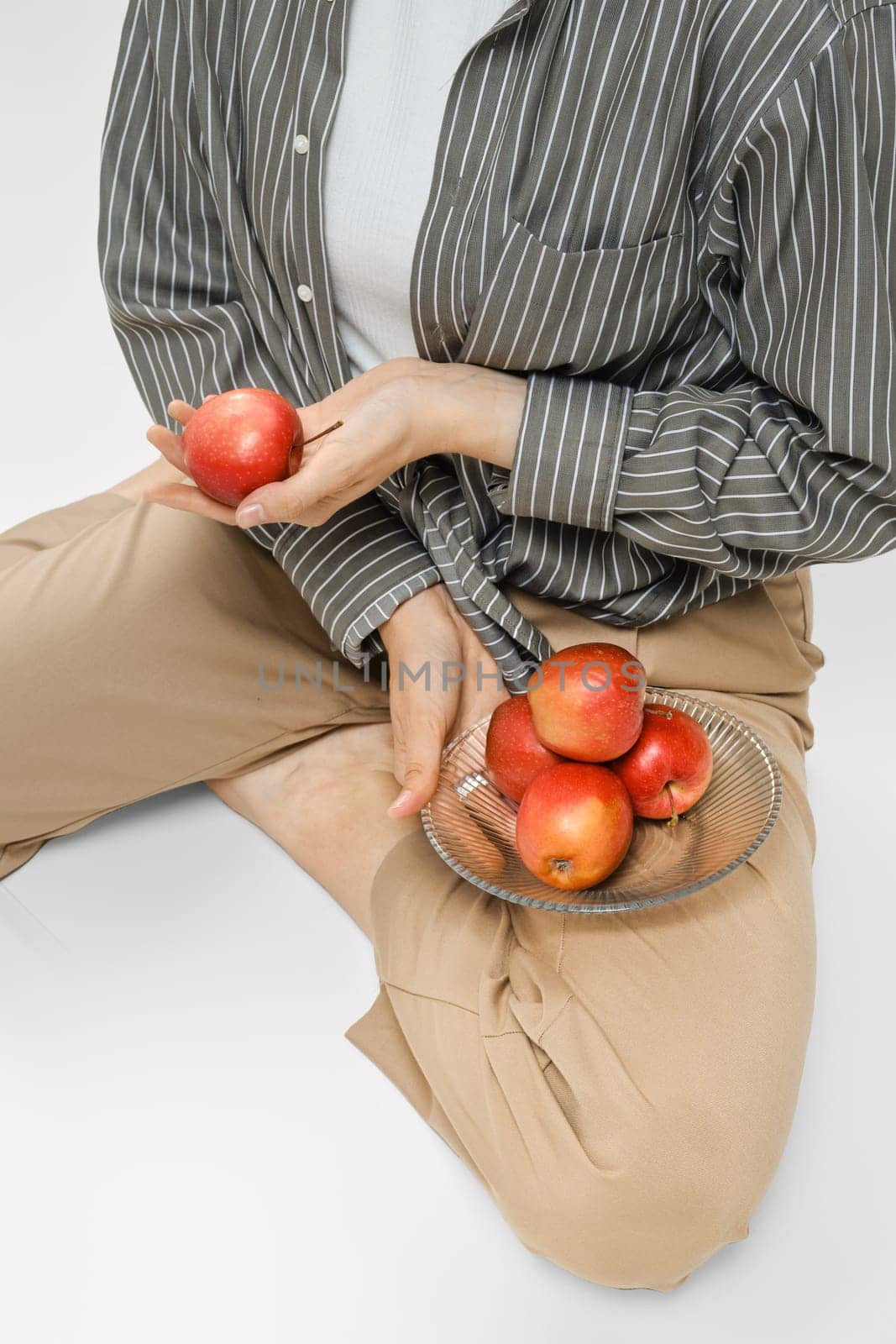 Unrecognizable woman put a plate with red apples on her hip and holding one apple in hand
