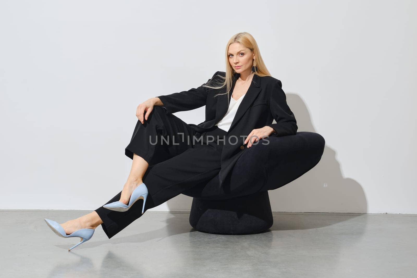 Modern successful businesswoman in black pantsuit sits on black bean bag indoors