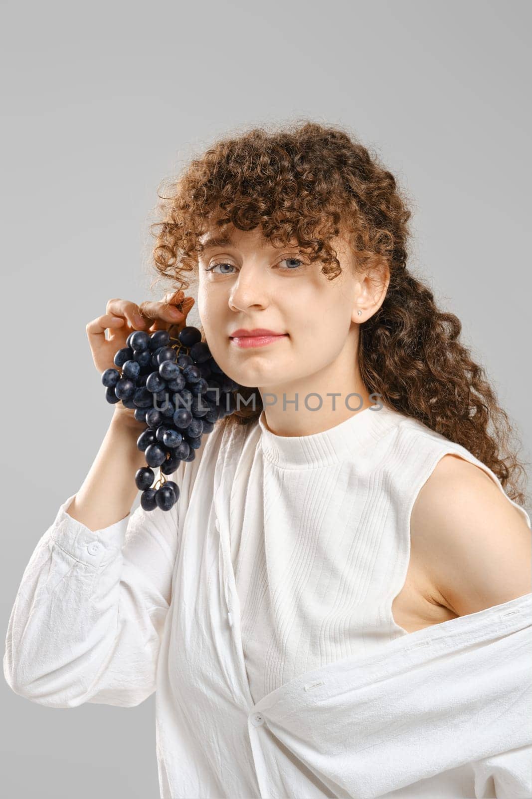 Young playful woman putting a bunch of grapes to her ear