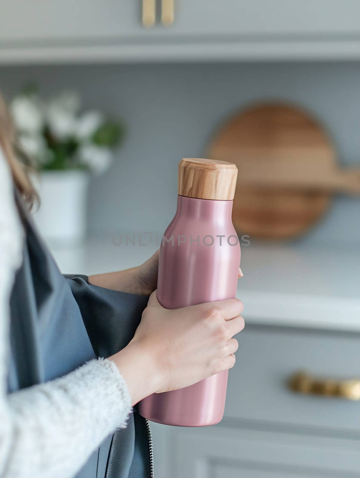 A woman stands in a contemporary kitchen, holding a pink water bottle with a wooden lid, surrounded by stylish decor.