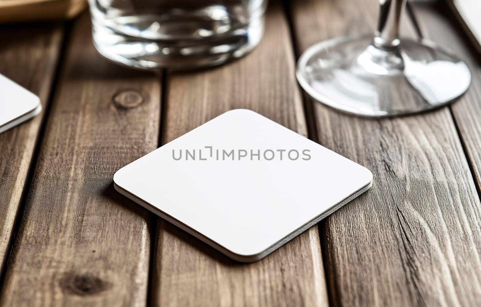 A simple white coaster rests on a rustic wooden table next to a glass and a wine glass, creating a cozy dining ambiance.
