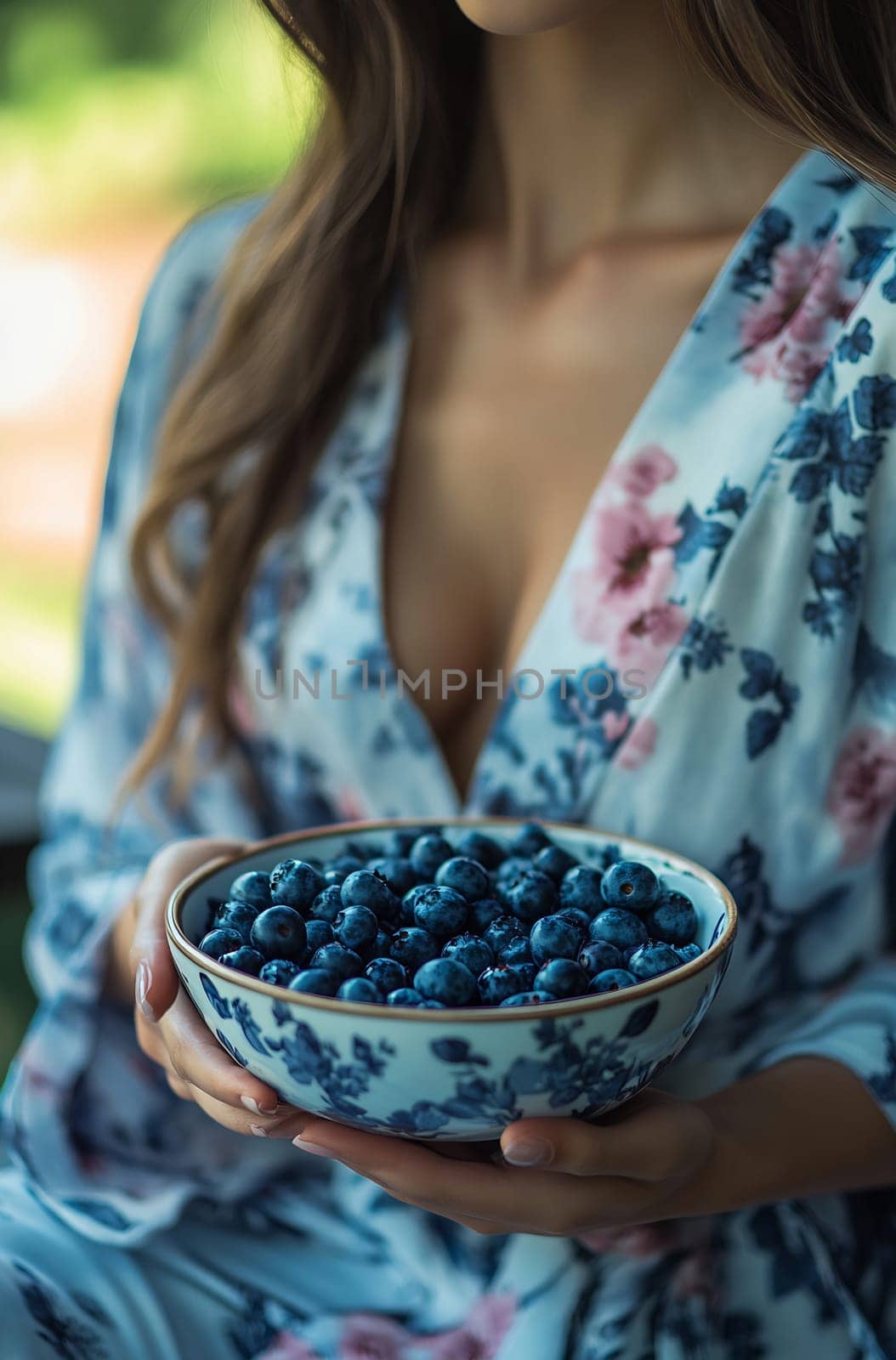 A woman in a floral robe holds a bowl filled with fresh blueberries while enjoying a bright indoor space.