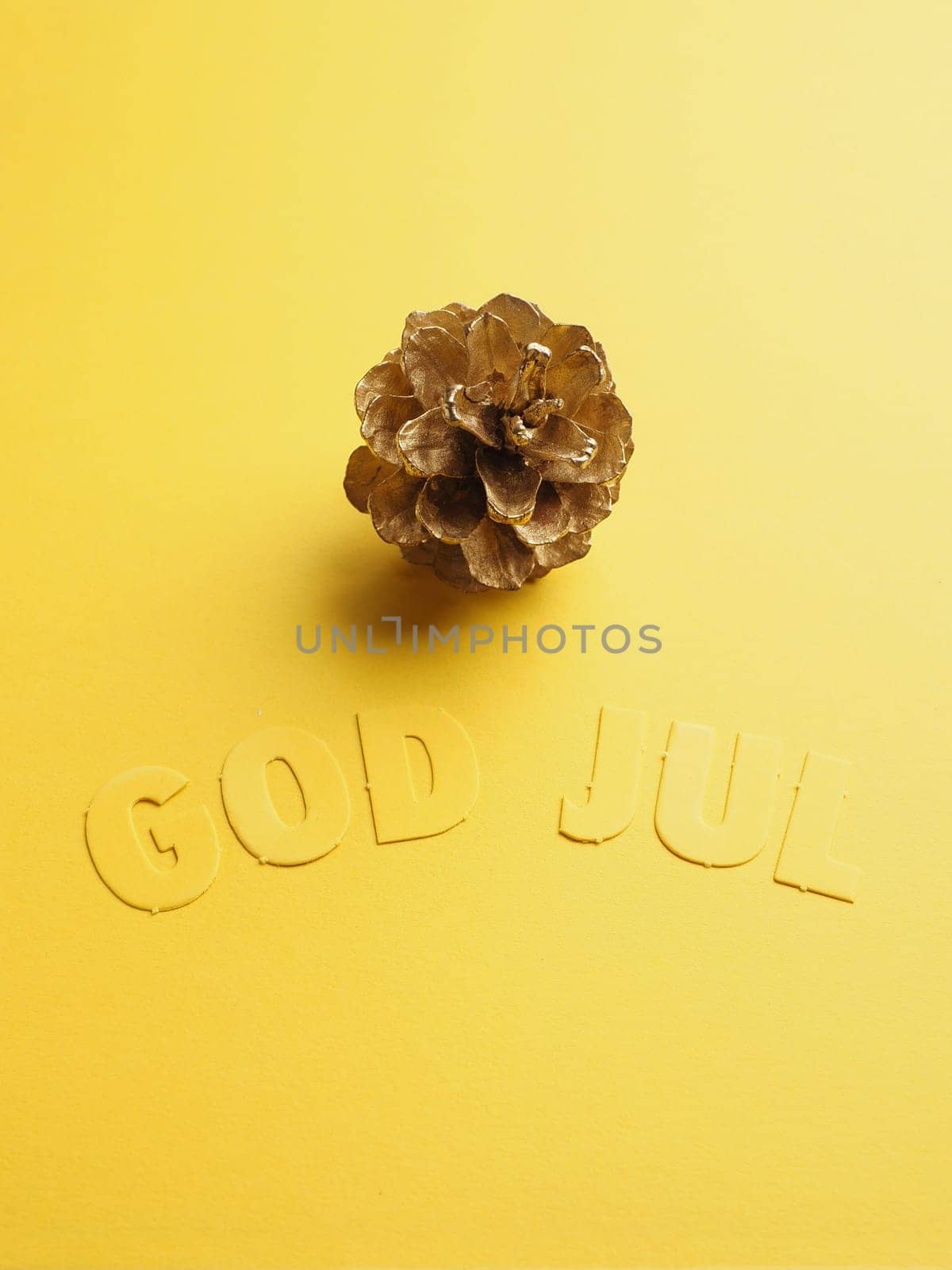 Yellow Christmas decoration with golden pine cone and the Scandinavian words God Jul, Scandinavian Merry Christmas