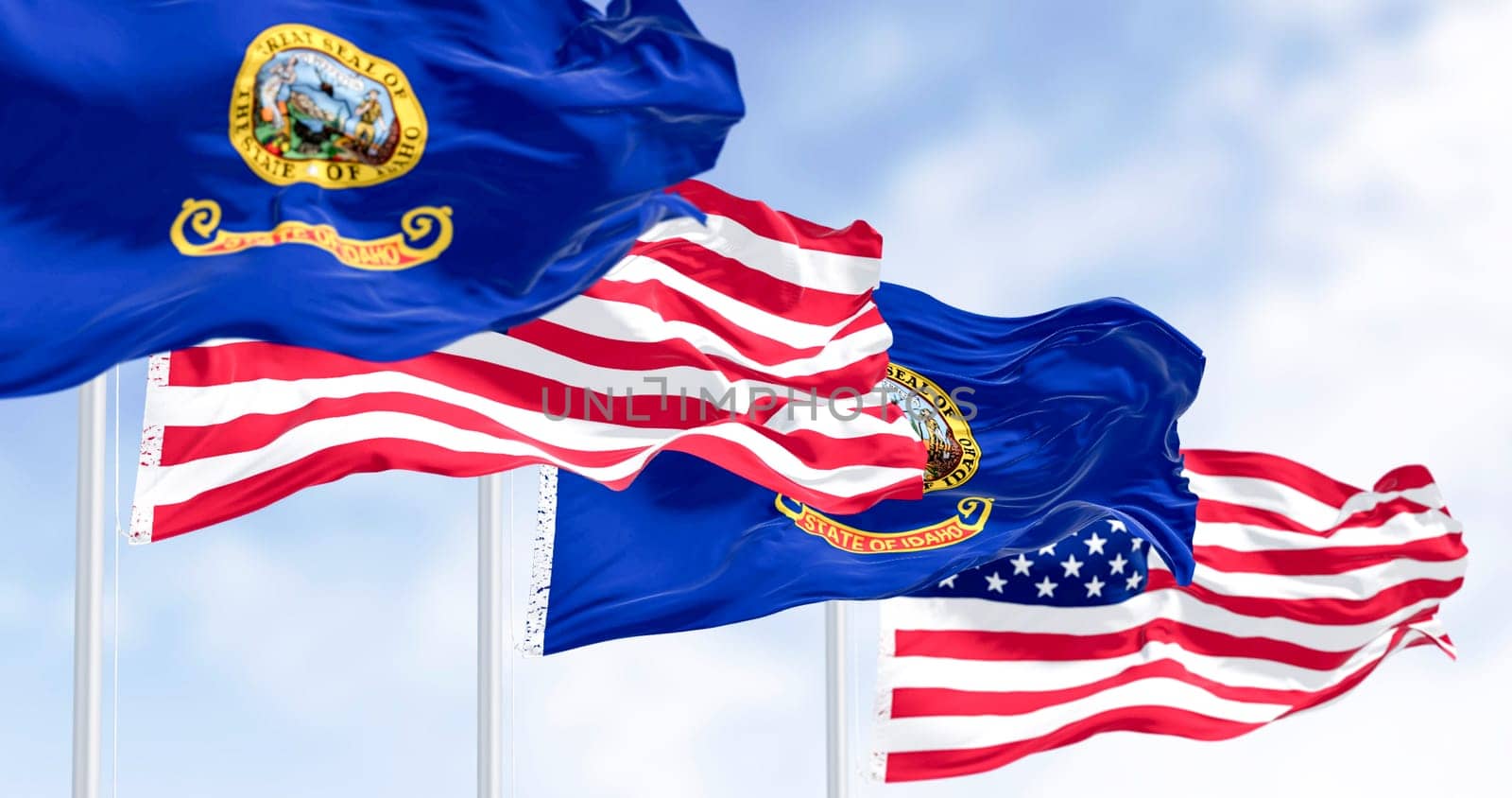 Idaho state flags waving along with the national flags of the United States of America on a clear day. 3D illustration render. Rippled fabric. Selective focus