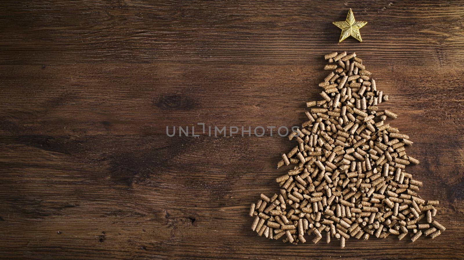 A top-down view of wood pellets meticulously arranged in the shape of a Christmas tree on a rustic wooden background. The selective focus enhances the texture of the pellets and the natural warmth of the wooden surface, creating a cozy and festive holiday atmosphere.