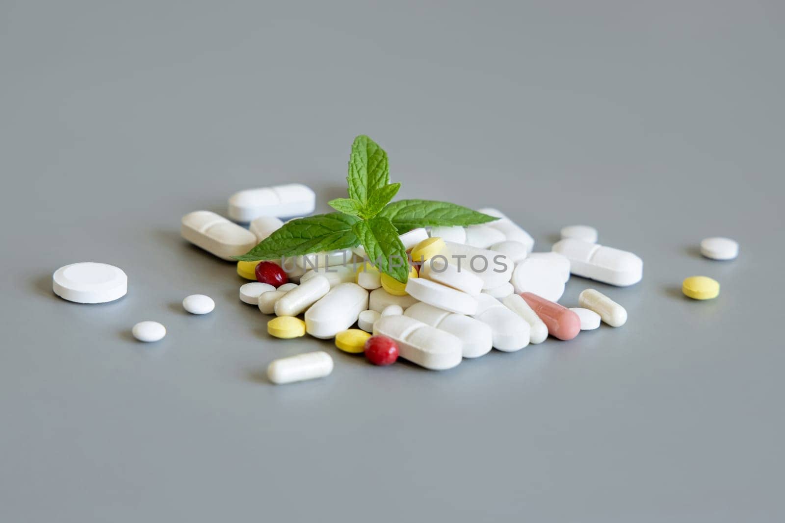 Pile of mixed medical pills with mint leaves above on grey close up. Medicinal treatment. Taking dietary supplements and vitamins. Assorted pharmaceutical products
