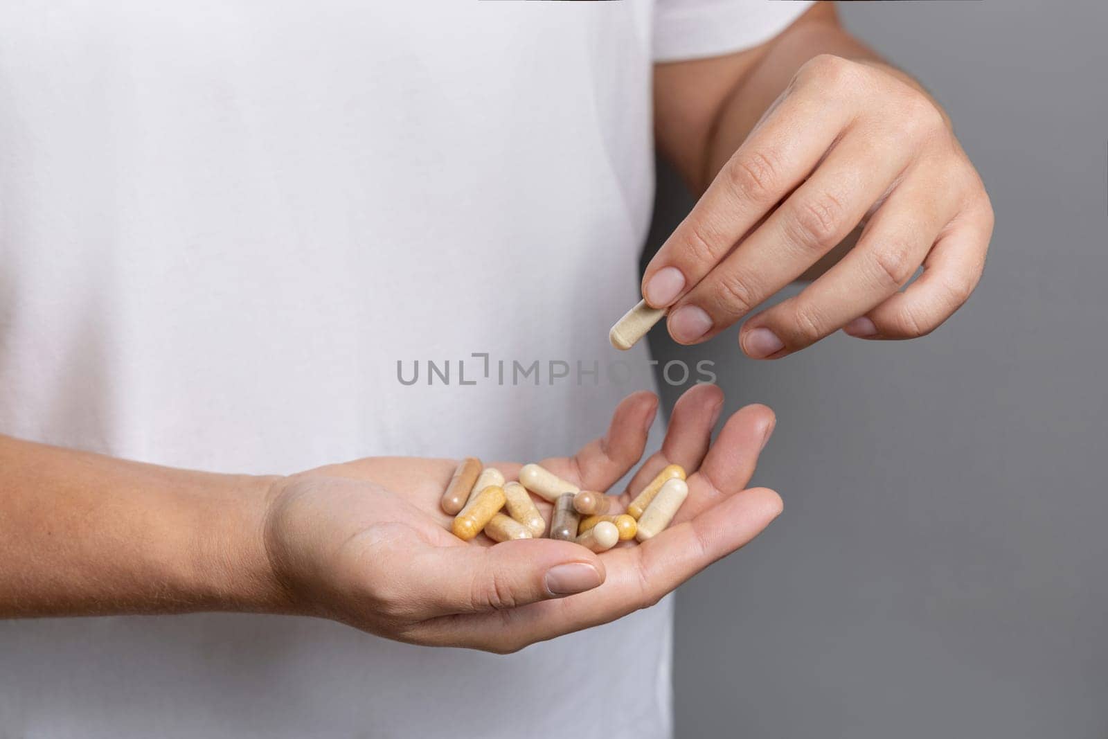 Woman holding in hands beige medical capsules closeup over white shirt and taking one capsule with fingers. Alternative herbal products for health care