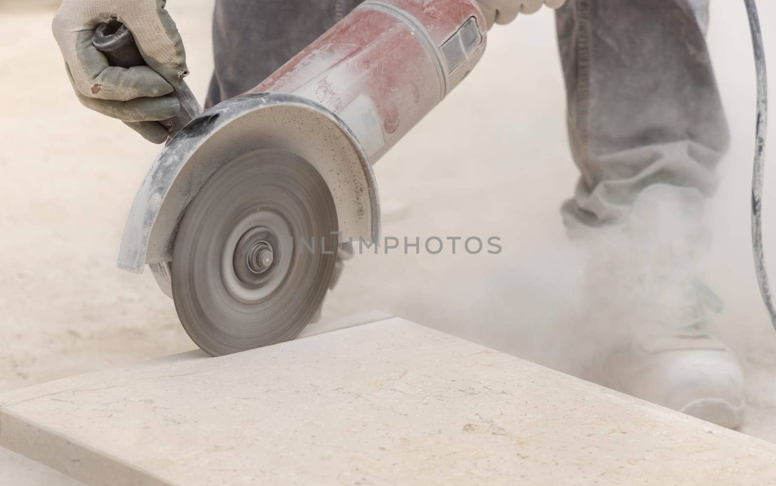 Craftsman cutting marble with circular saw piece against scaffoldings. Men in dusty grey work clothes and white construction helmet during construction process