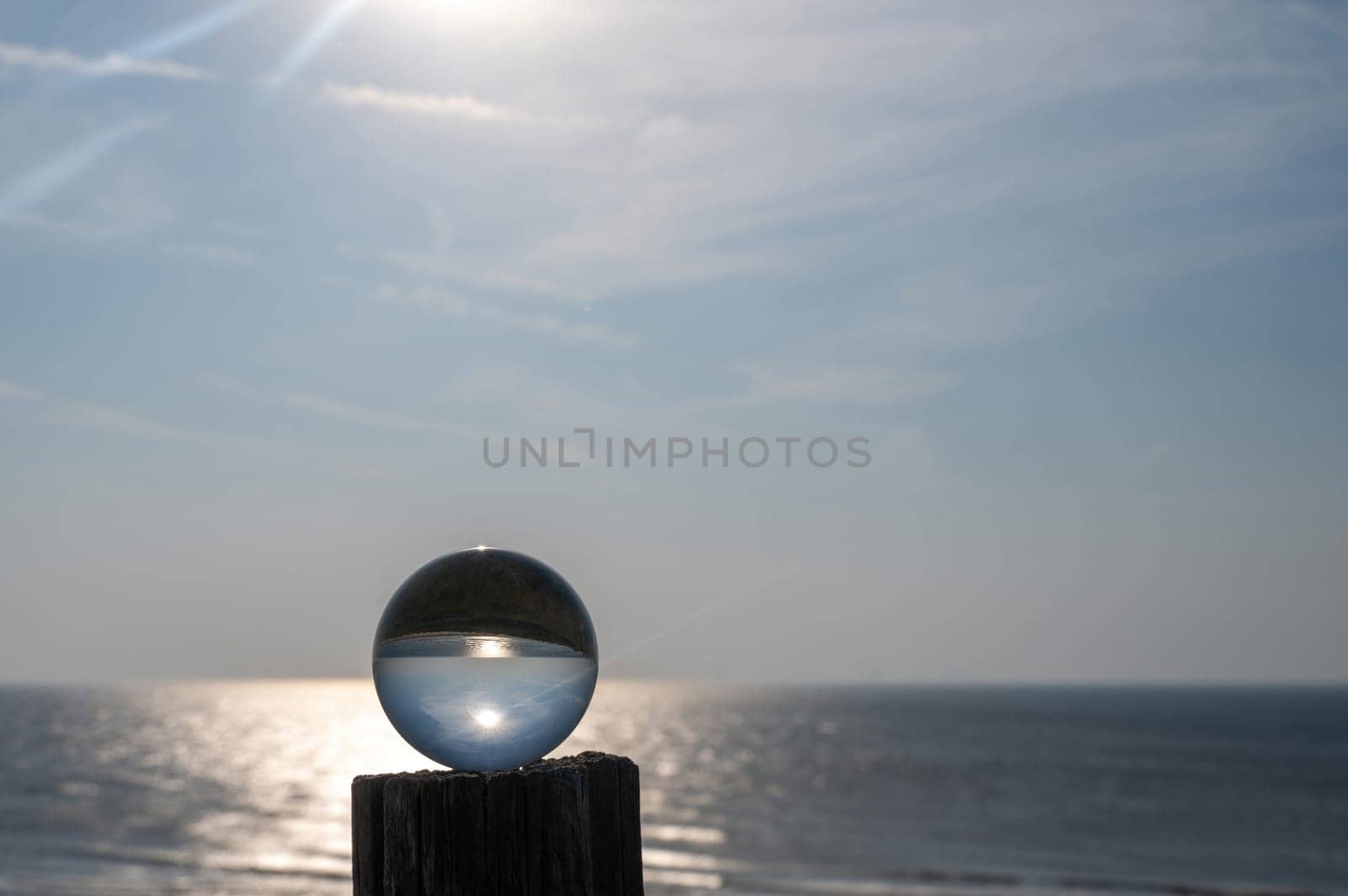 Glass ball lies on a wooden post, in the ball the sea, the sun and the blue sky are reflected