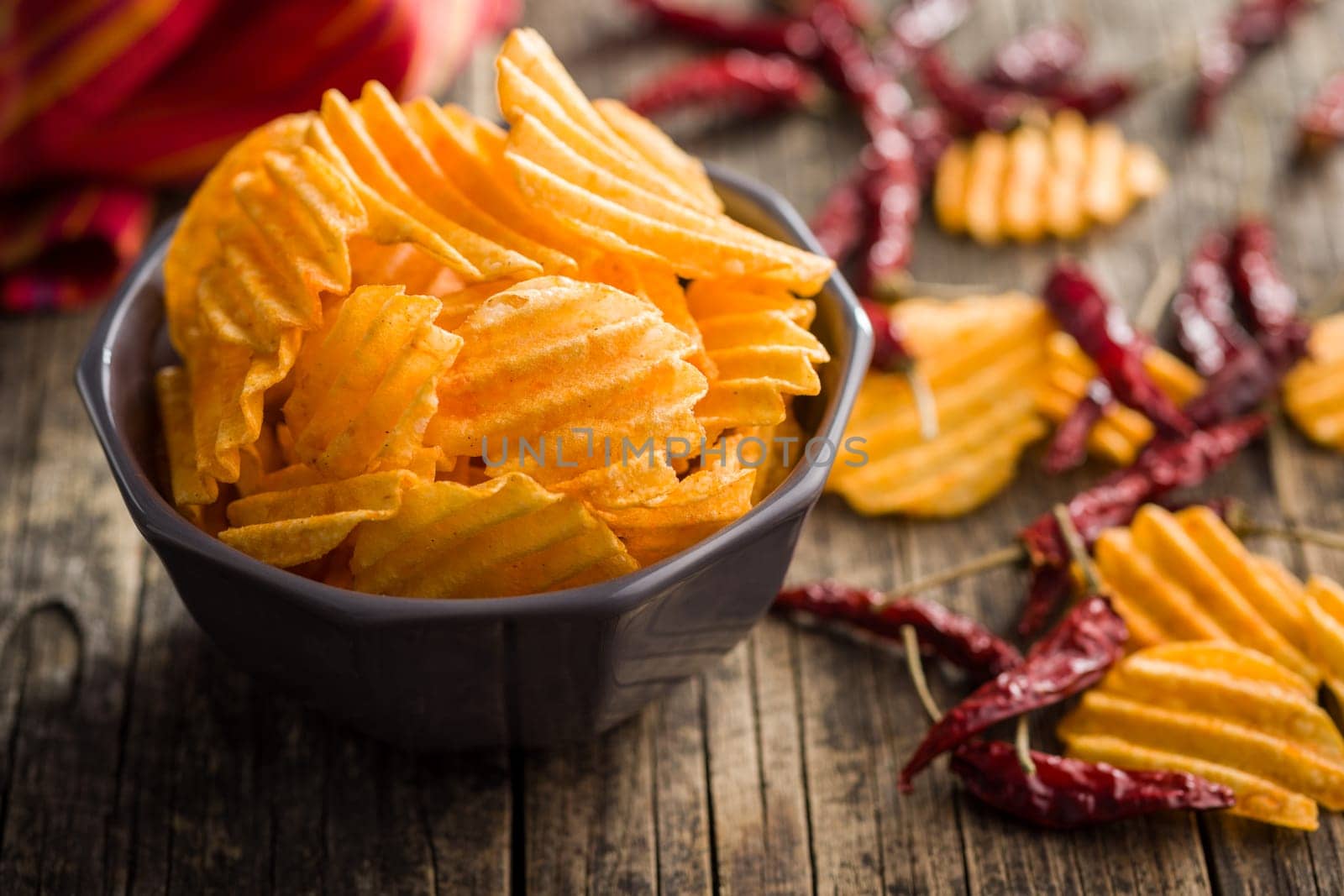 Crispy potato chips in bowl on a wooden table.