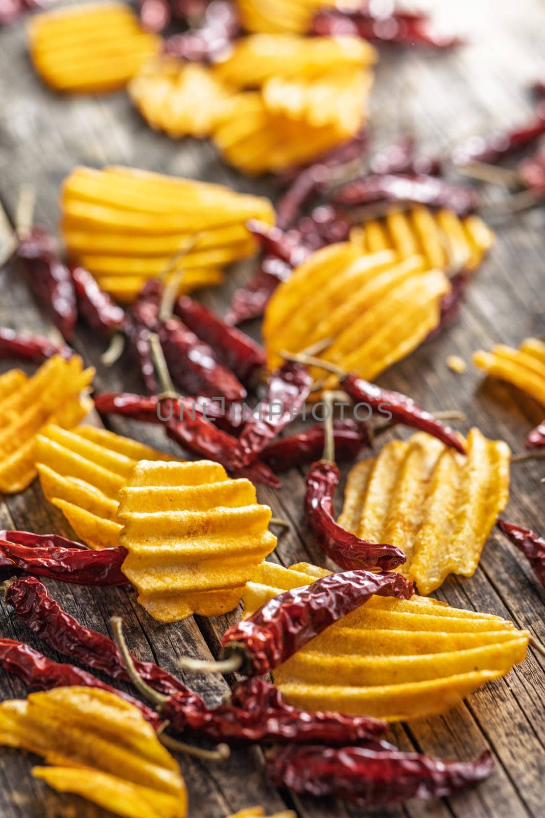 Crispy potato chips and chili peppers on a wooden table.