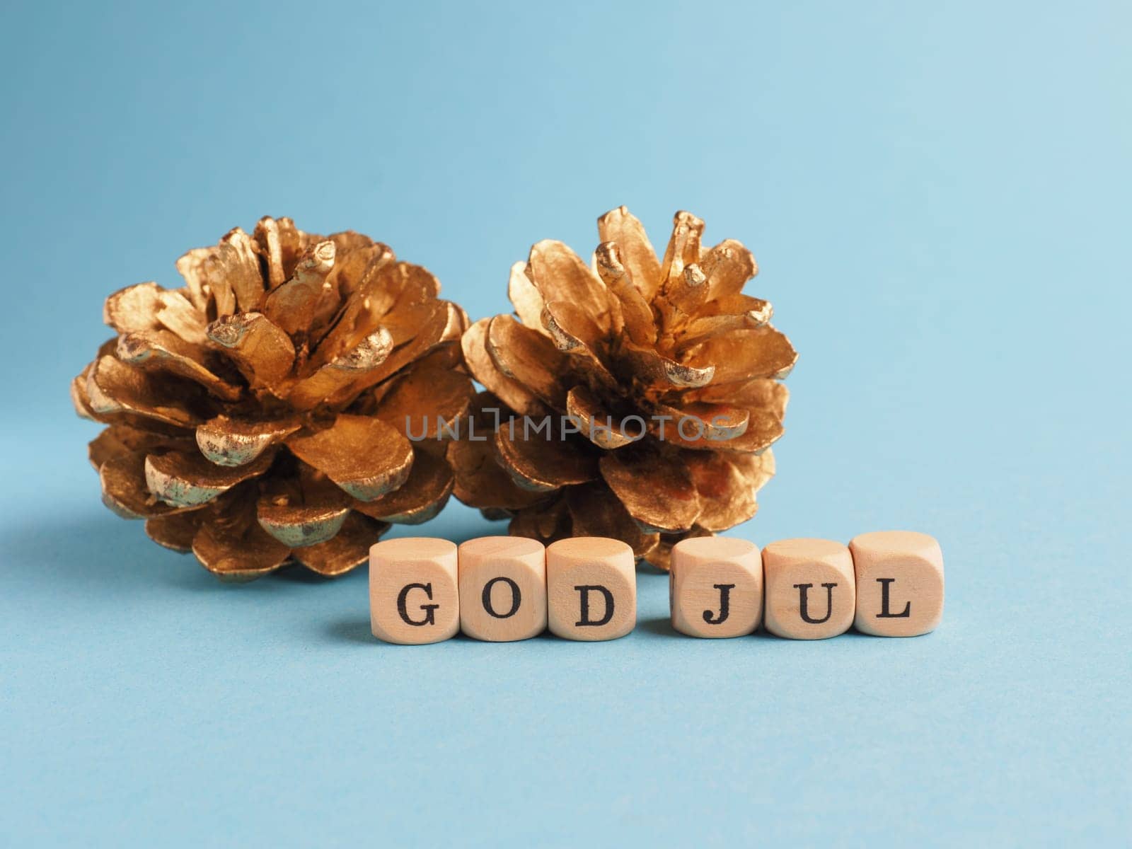 Golden pine cones with wooden blocks and the words God Jul, Scandinavian Merry Christmas on a blue background