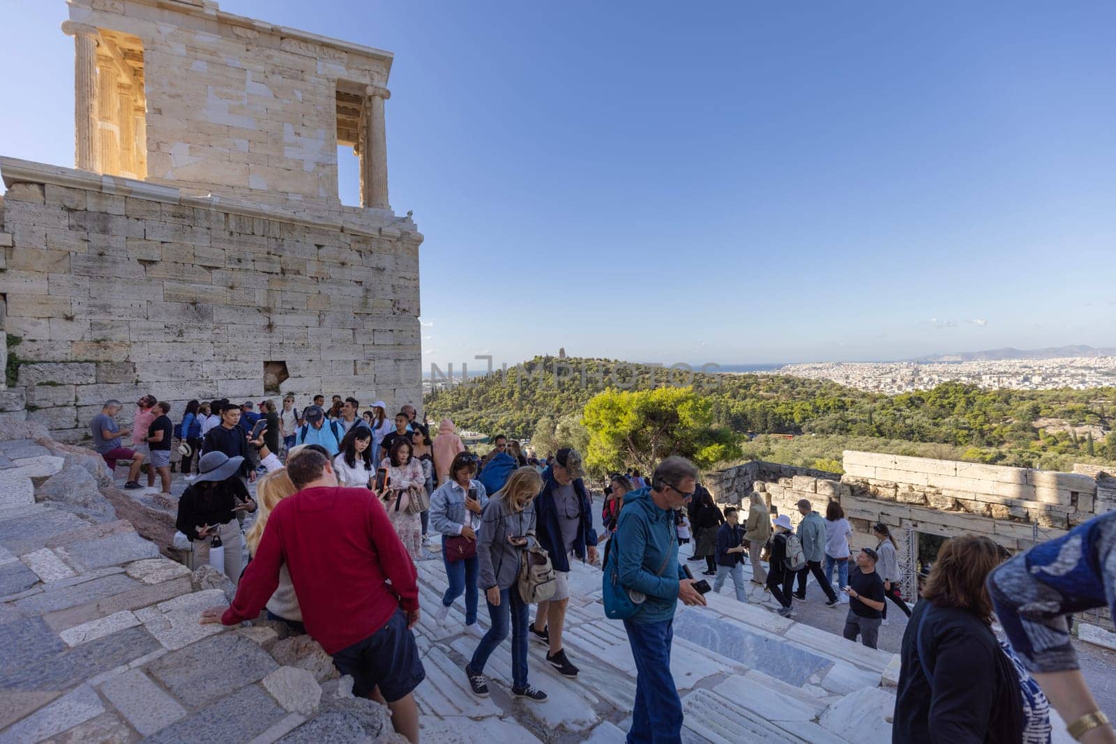 Athens, Greece - October 17, 2022: Crowd of tourists in front of monumental ceremonial gateway Propylaia to Acropolis of Athens. Remains of Temple of Athena Nike