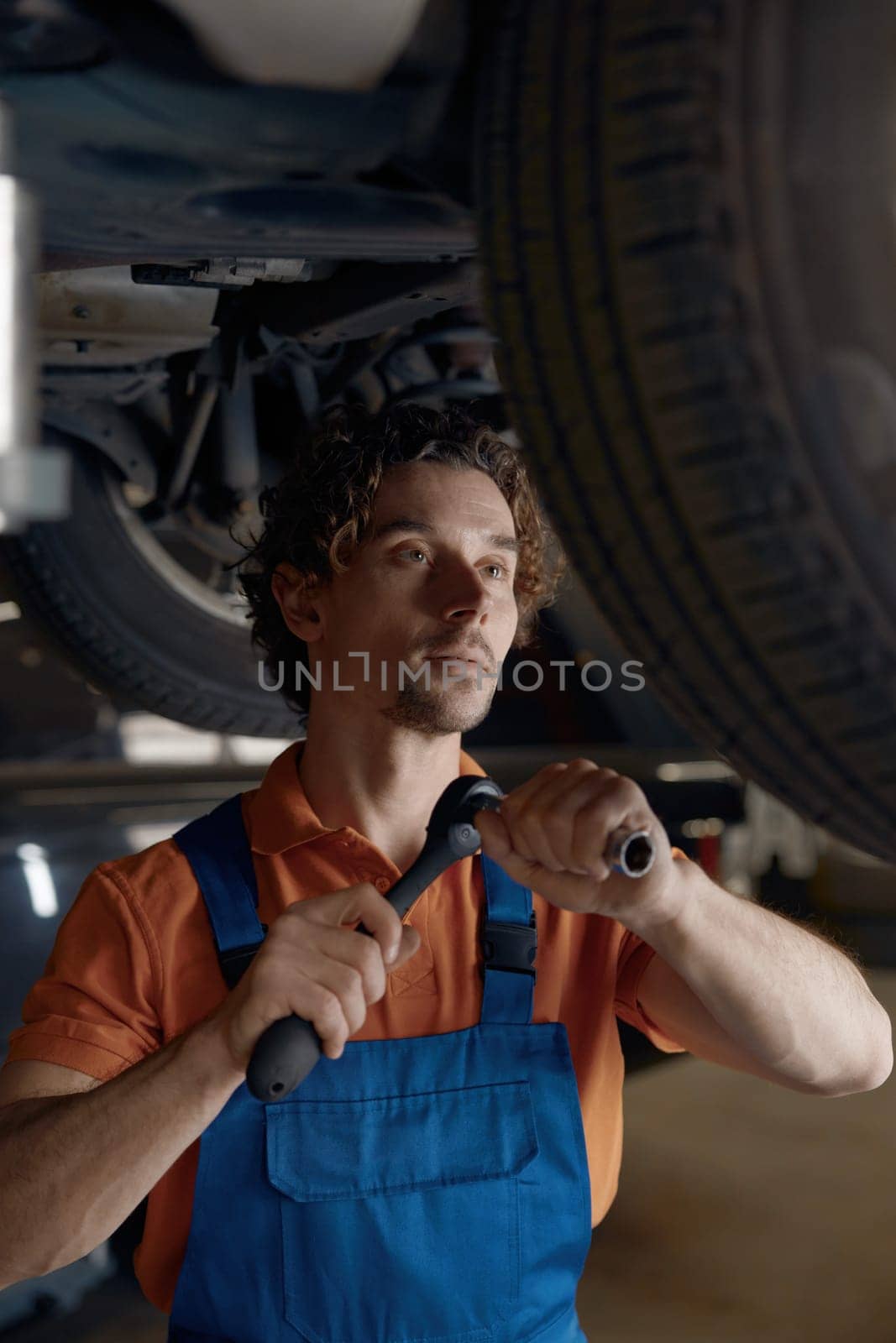 Professional mechanic repairing wheel fixing problem standing under car. Auto repairman checking springs and shocks in garage