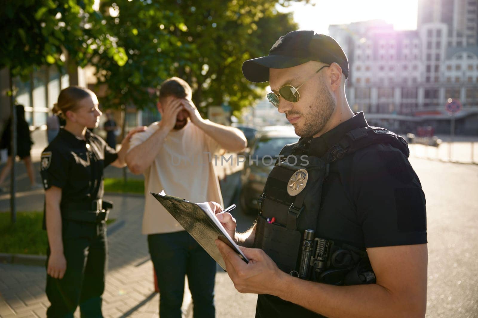 Policeman filling out offense form, while policewoman calming down upset male citizen victim after unfortunate incident on city street