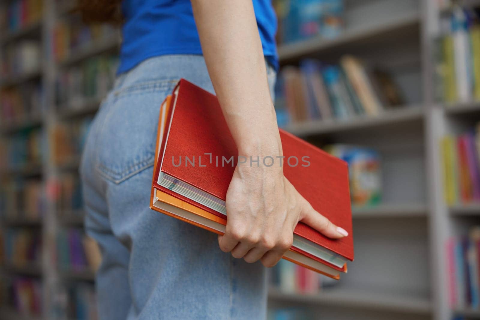 Closeup view on female hands holding pair of books over bookshelves on background. Knowledge, cognition, education and research concept