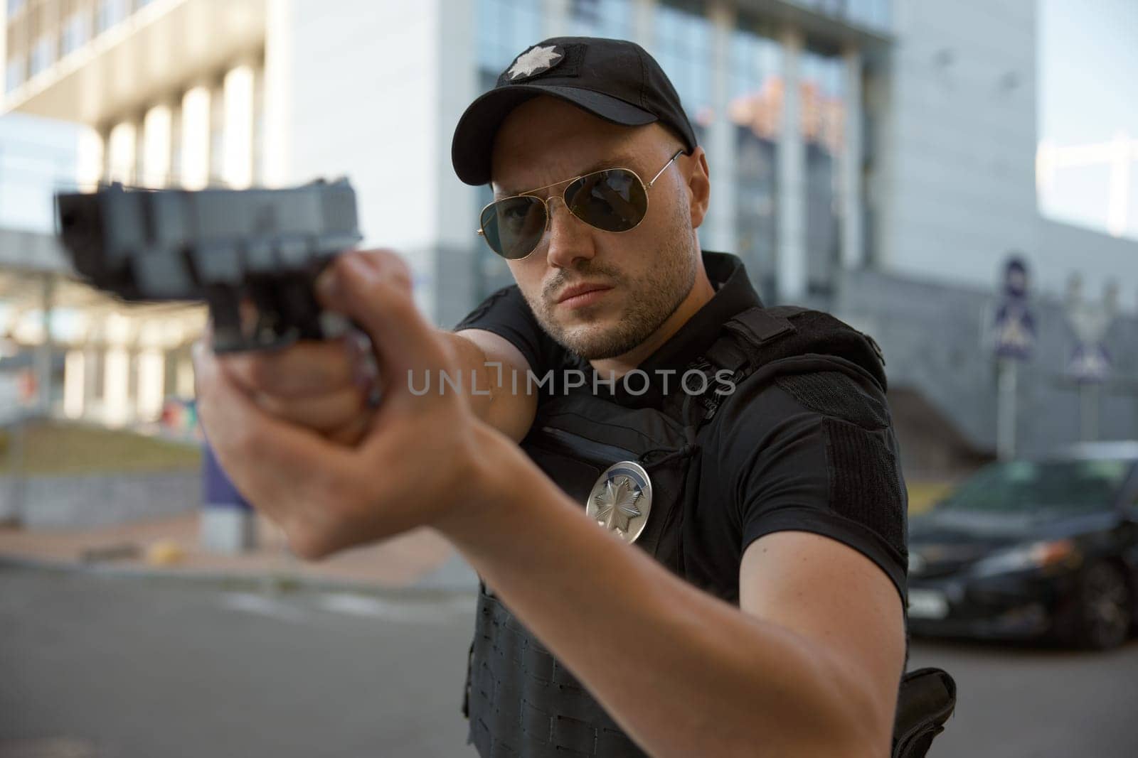 Portrait of concentrated man patrol police officer aiming with handgun in action standing outdoors in city street