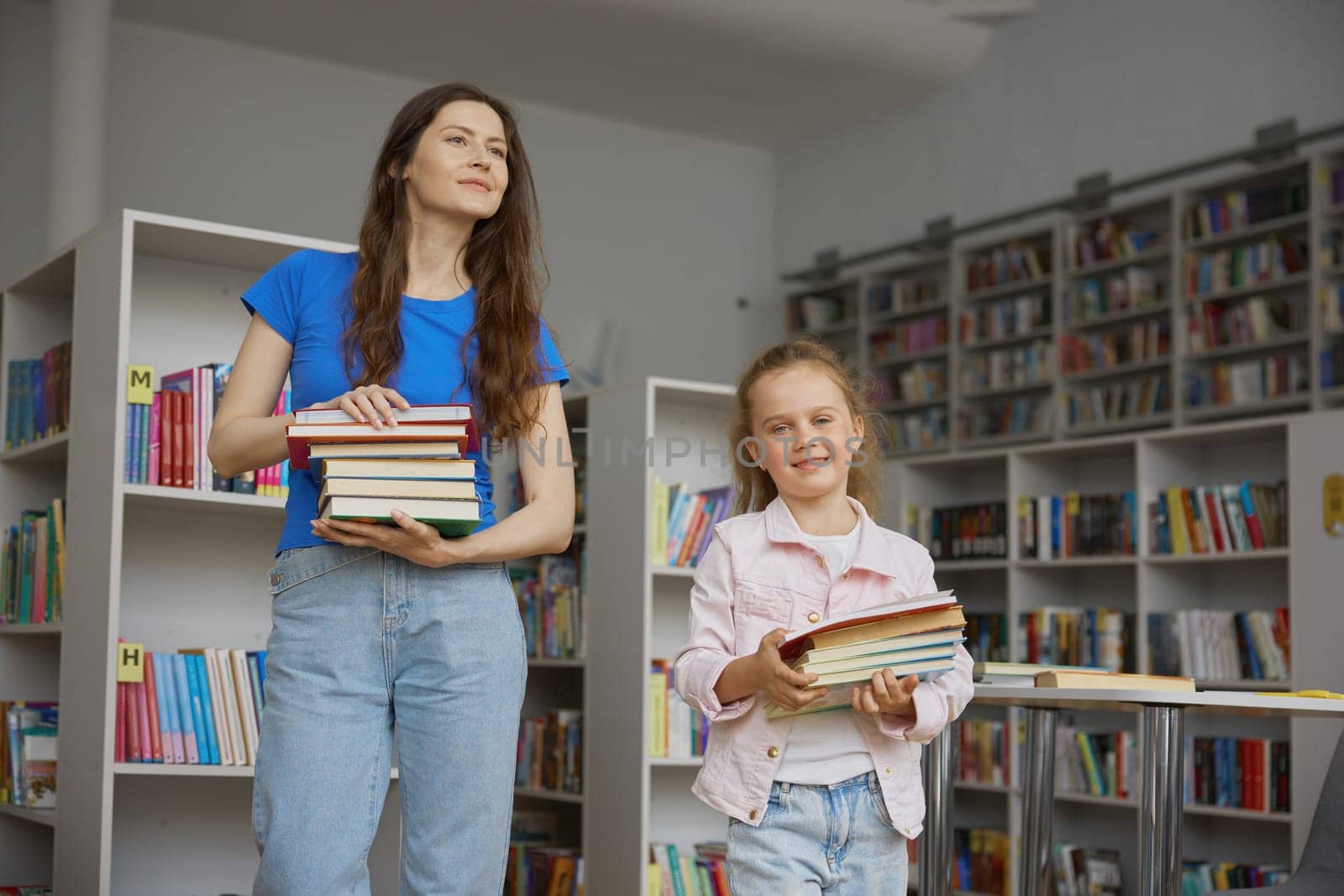 Happy family doing shopping at bookstore. Mother and daughter carrying books in stack preparing for studying