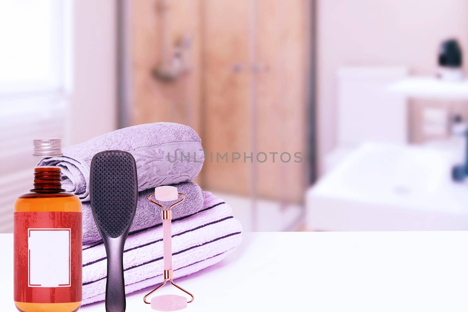 Spa, body, beauty and wellness concept. Various towels, a jade facial roller, a stylish hair brush and a bottle of shampoo over abstract blurred bathroom. Copy space.