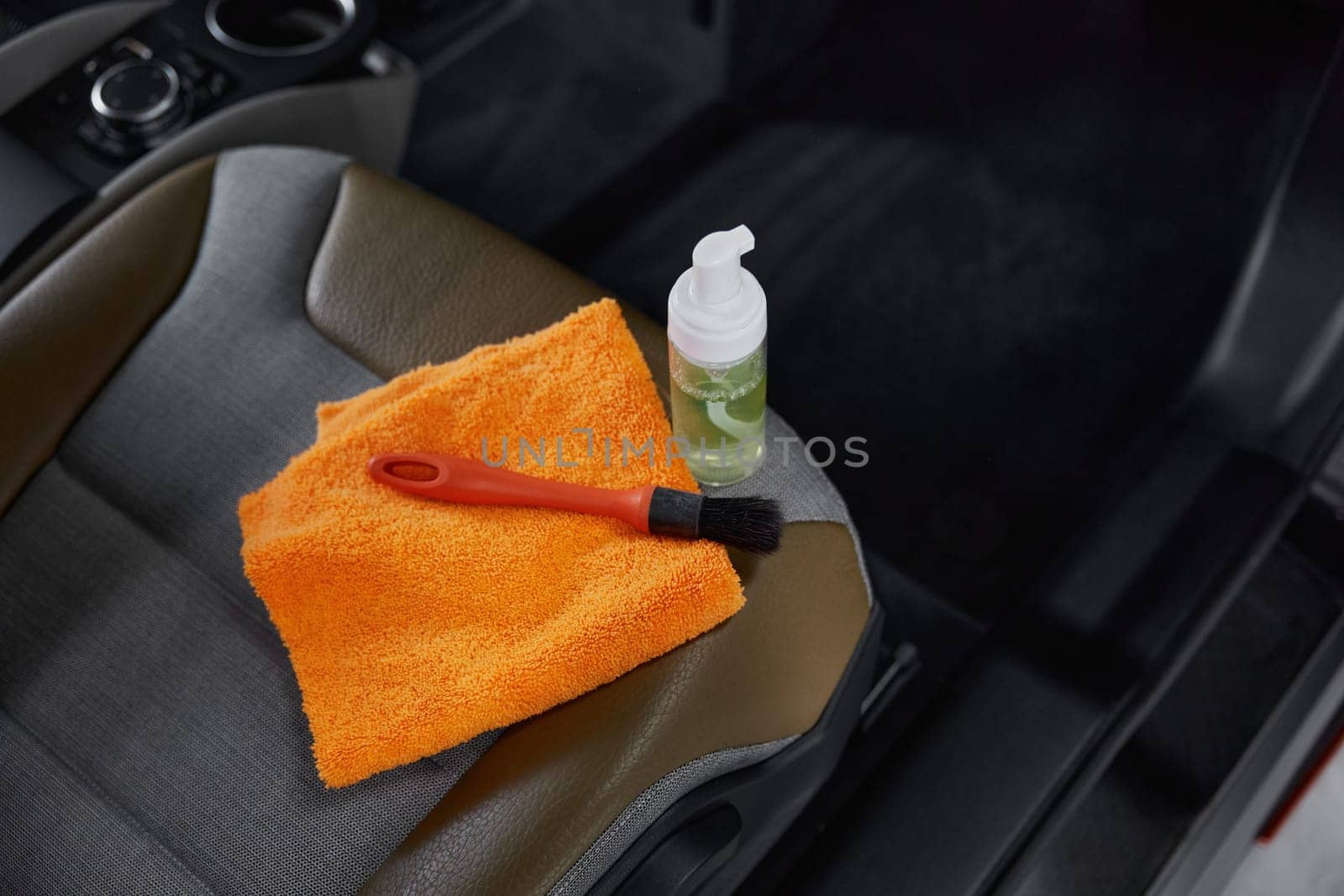 Cleansing brush towel and detergent in disinfectant spray bottle on front passenger seat high angle view closeup. Car detailing concept