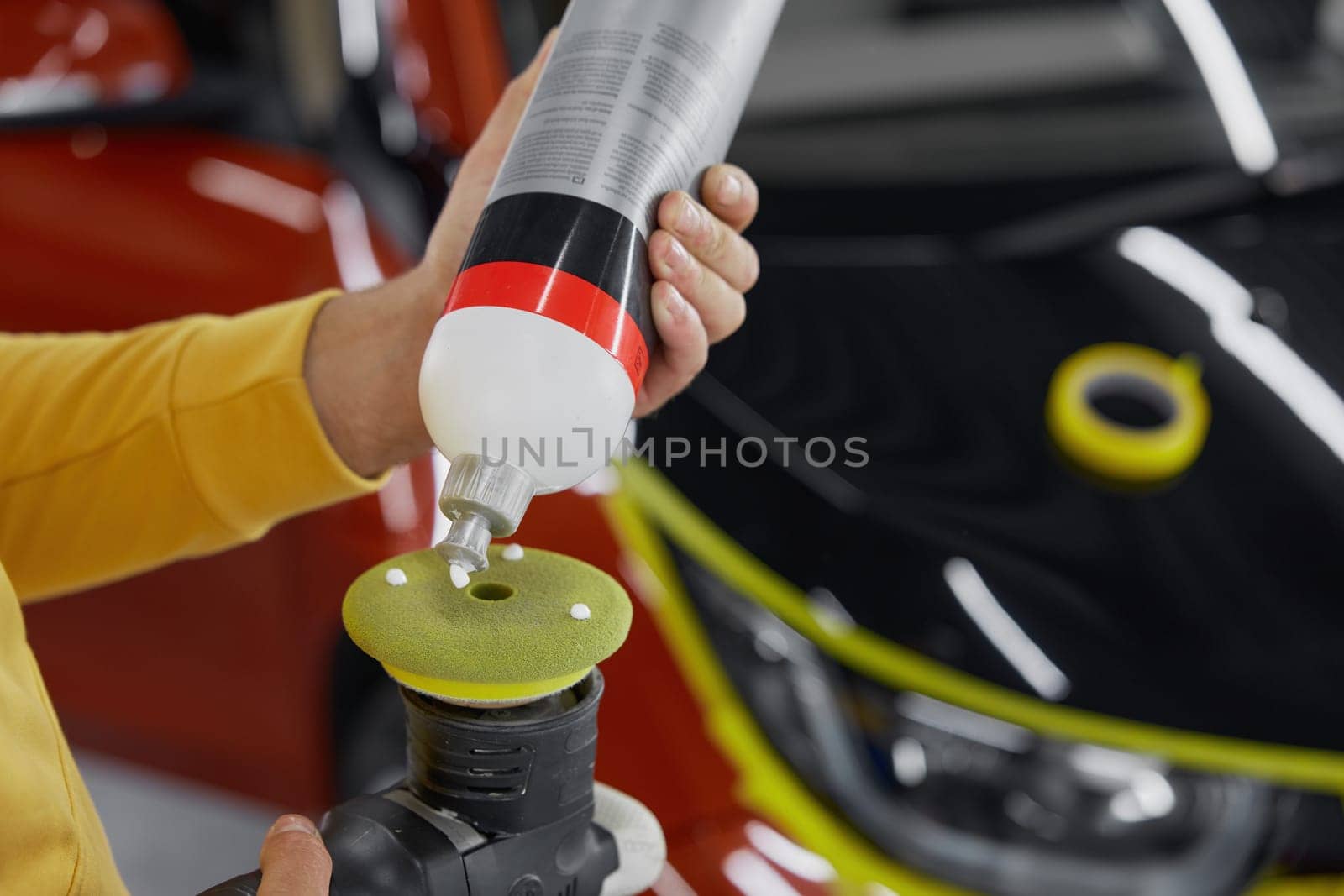 Closeup man worker squeezing out special paste from bottle onto polishing hand power tool nozzle
