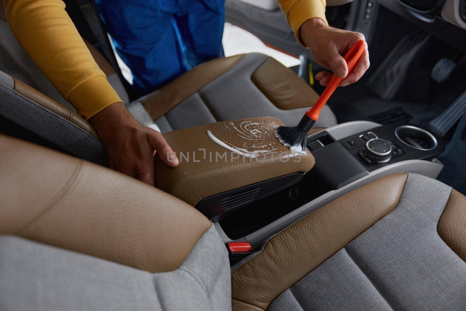 Autoshop worker cleaning car interior with detergent foam and brush. Car cleansing and detailing service