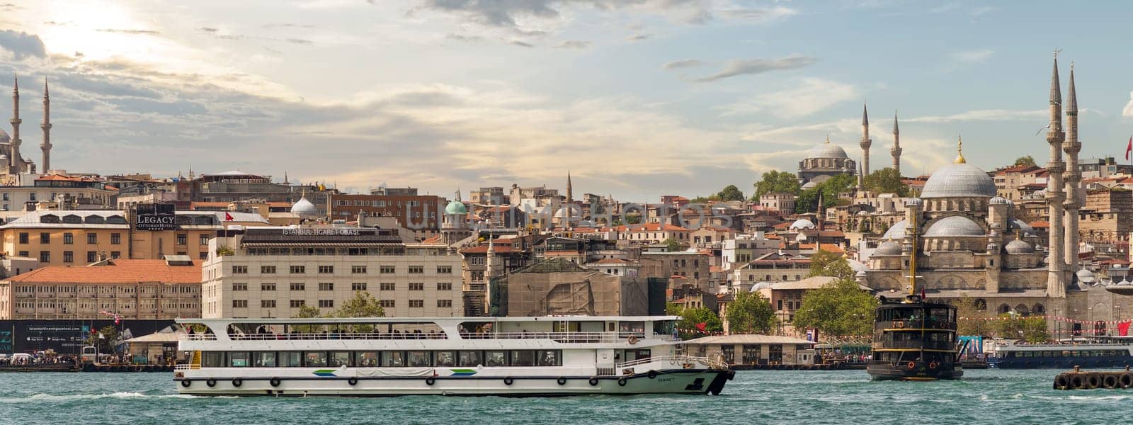 Istanbul, Turkey - May 13, 2023: A ferry cruises along the Bosphorus Strait as the sun sets, highlighting Istanbul's iconic skyline filled with historical architecture and minarets