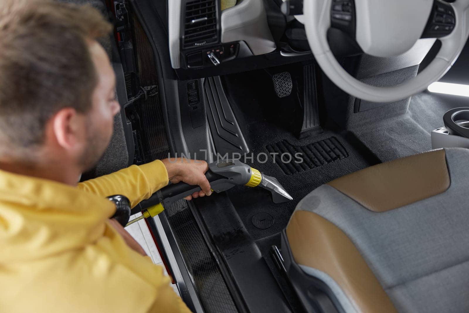Car wash service worker vacuuming dust and dirt form back passenger seats applying professional equipment