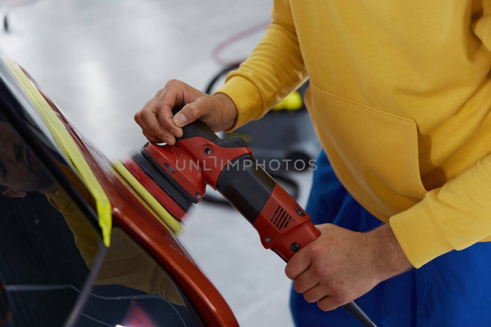 Auto master using rotary grinder for polishing car body parts. Automotive detailing service