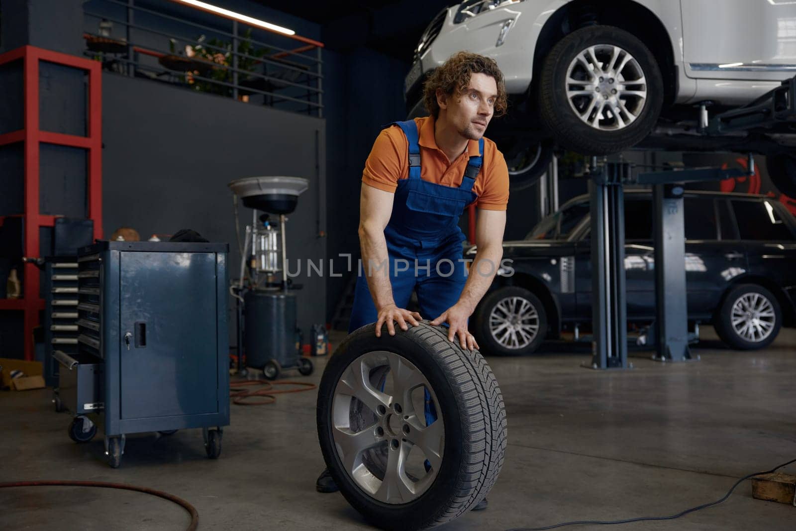 Repairman rolling car spare tire while working on wheel replacement providing professional automotive mechanical