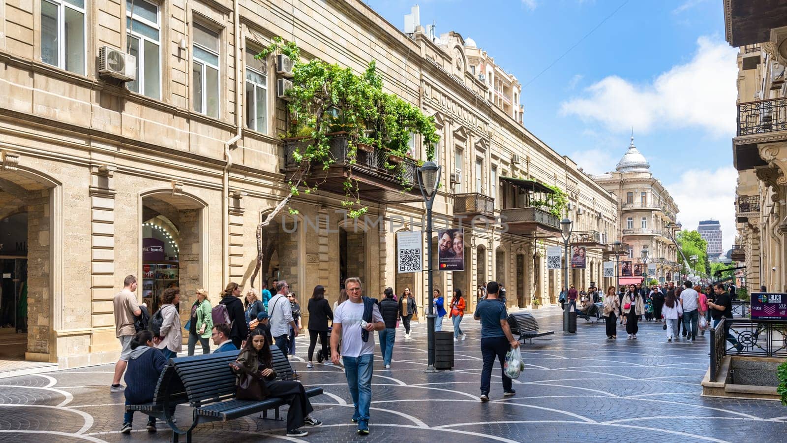 Baku, Azerbaijan - May 5, 2024: Nizami Street bustles with activity as pedestrians stroll under a clear blue sky. Lush greenery adorns the balconies, enhancing the vibrant atmosphere