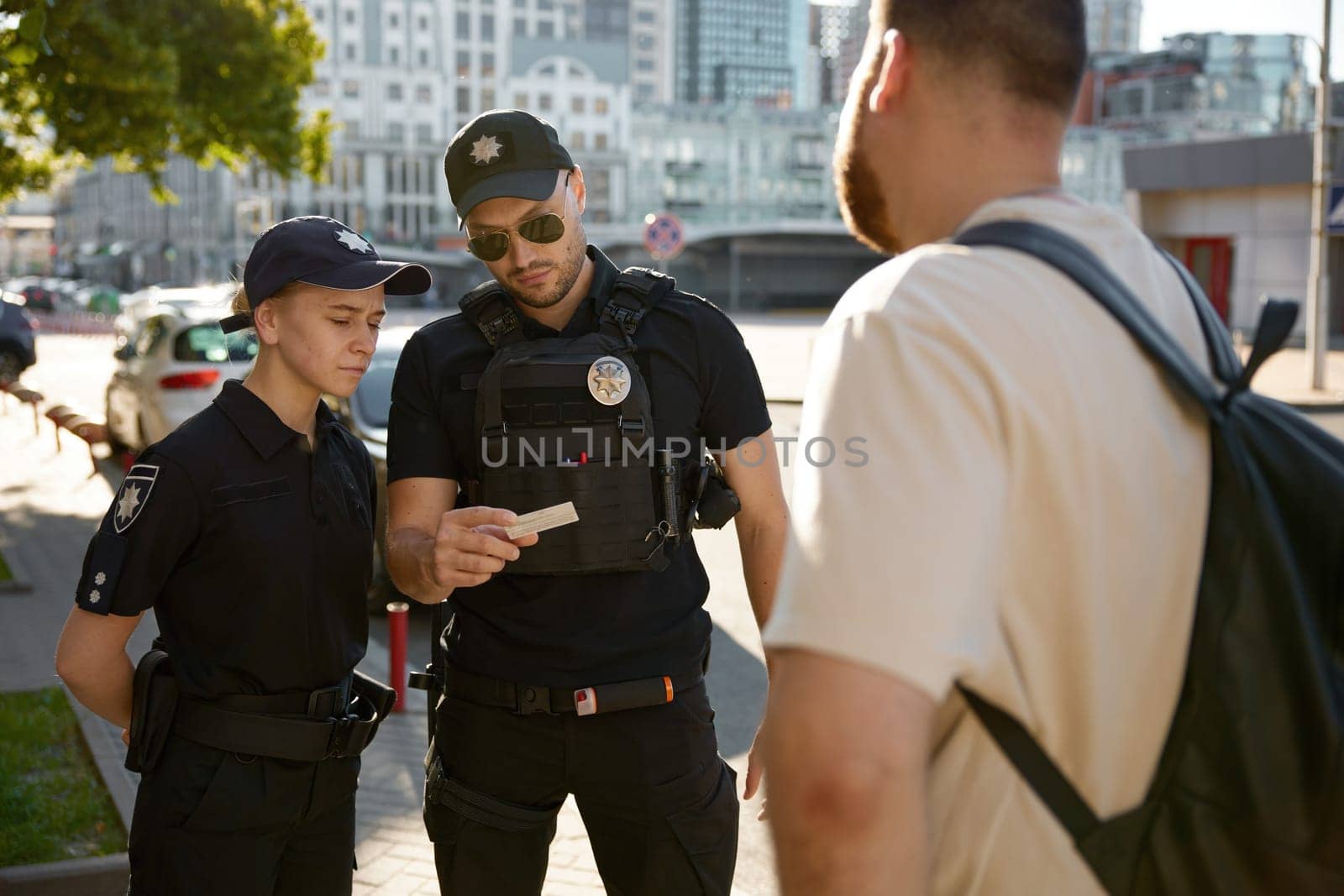 Serious patrol policeman and policewoman checking personal documents of citizen on city street