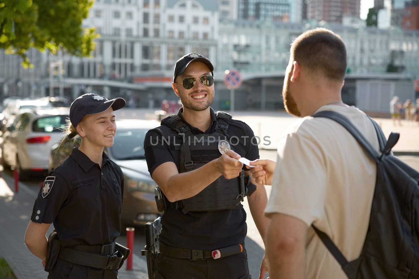 Friendly smiling patrol policeman giving back passport to citizen after checkup on city street. Law, order and protection of civilian