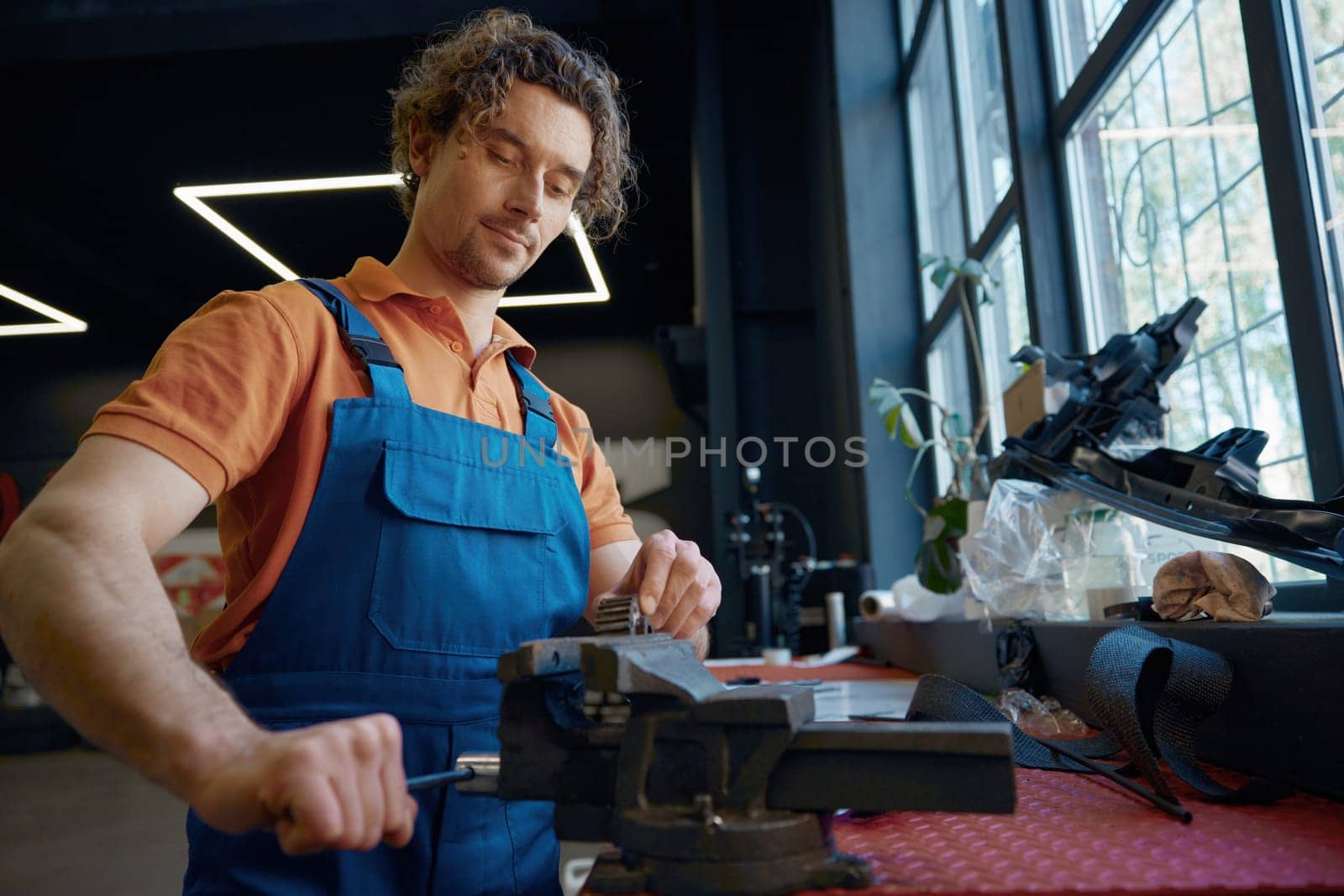 Auto mechanic using bench vice to adjust spare part at car repair garage. Automotive repairman everyday routine and professional occupation