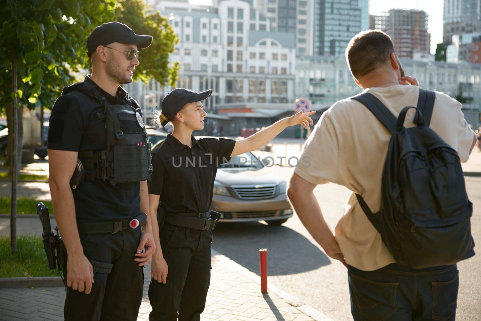 Patrol policeman and policewoman showing city way to citizen. Police officers giving directions to man tourist to place of destination