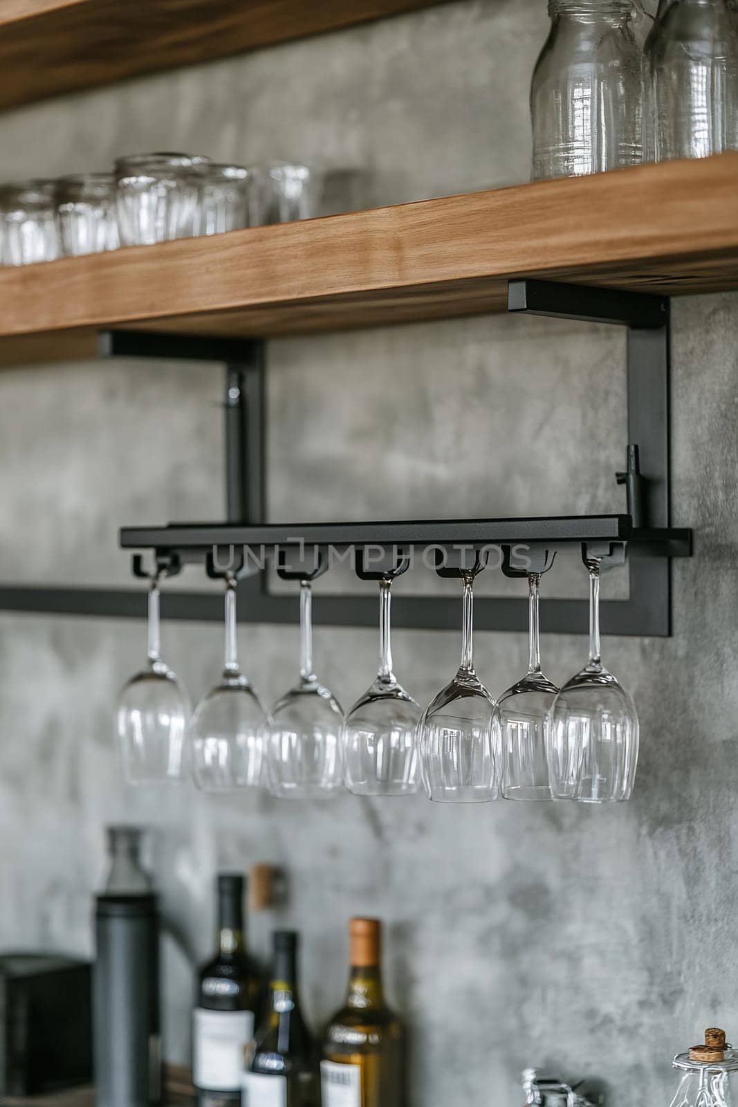 A stylish arrangement of wine glasses suspended from a sleek rack above a modern kitchen countertop with various bottles below.